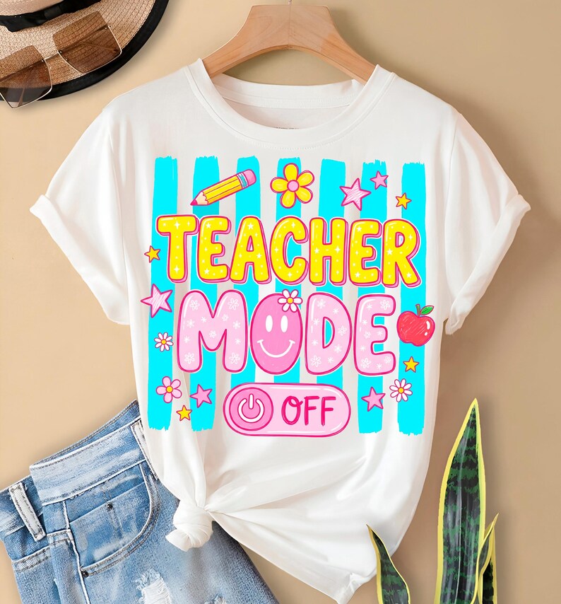 May include: White t-shirt with a colorful graphic design. The design features the words "TEACHER MODE" in yellow and pink, along with a smiley face, an apple, a pencil, and stars. The shirt has blue vertical stripes.