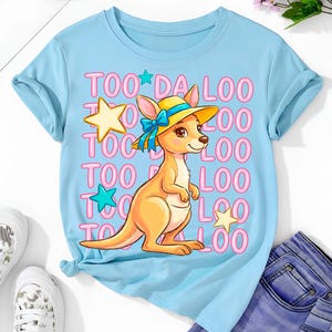 Op de afbeelding: Lichtblauw T-shirt met een cartoon kangoeroe met een gele hoed en een blauwe strik. Het shirt heeft de tekst "TOO DA LOO" in roze letters en sterren. Het shirt is gemaakt van een zacht materiaal.