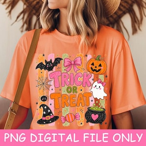 May include: An orange t-shirt featuring a Halloween graphic with the text Trick or Treat. The design includes a black bat, a pink bow, an orange jack-o'-lantern, a spider web, a white ghost, a black witch hat, a candy, and a black cauldron.