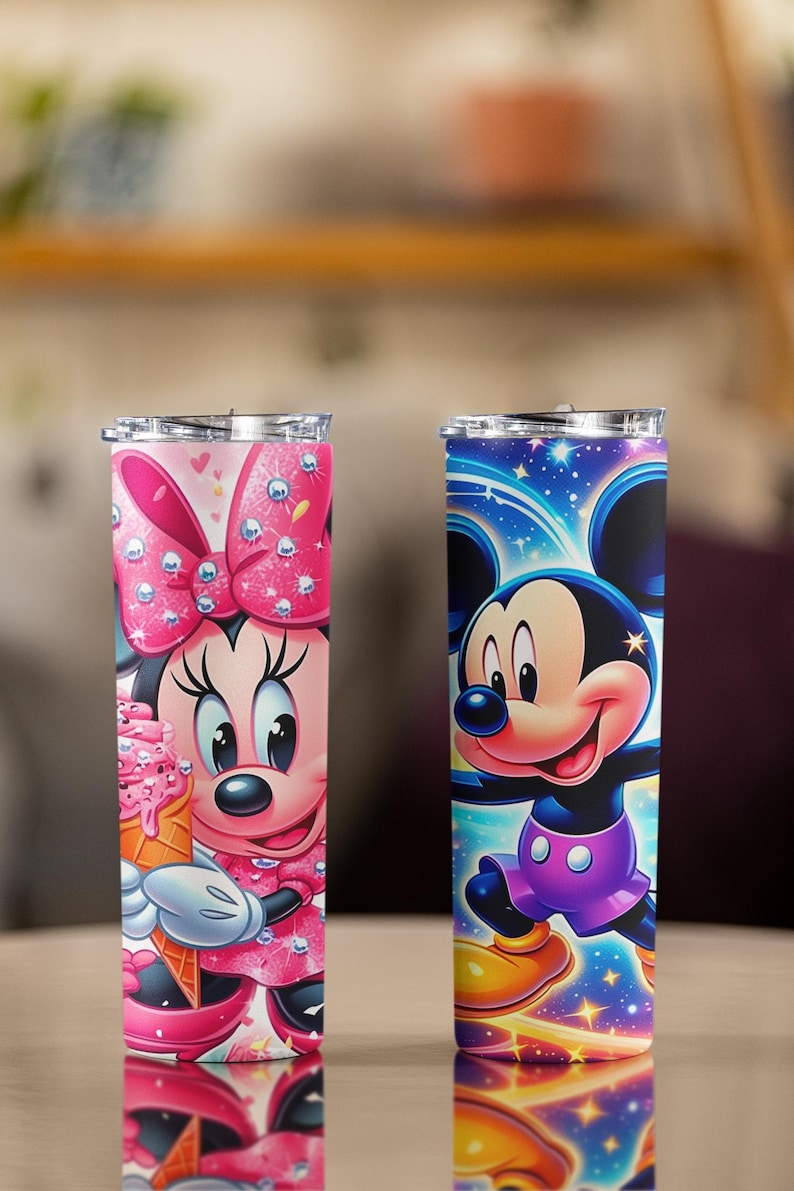 Peut inclure: Deux gobelets en acier inoxydable avec des personnages Disney. L'un pr&eacute;sente Minnie Mouse en rose avec un cornet de glace, l'autre Mickey Mouse en bleu et violet. Les deux gobelets ont des couvercles transparents et sont isol&eacute;s.