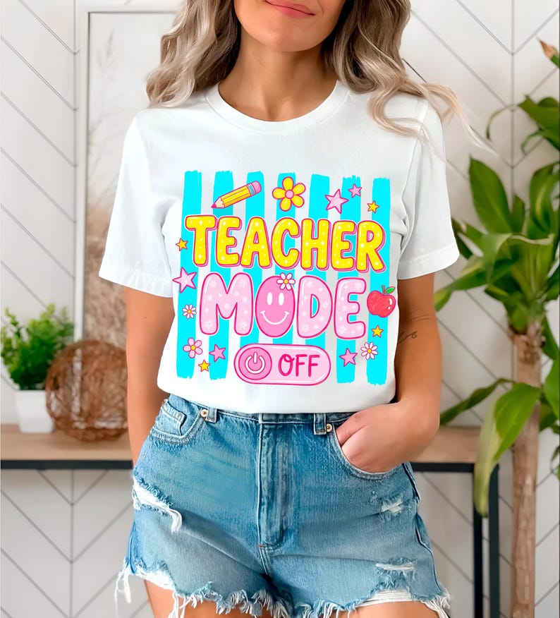 May include: White t-shirt with a colorful graphic that reads "TEACHER MODE OFF." The design includes a pencil, flowers, stars, an apple, and a smiley face. The shirt has a crew neck and short sleeves.
