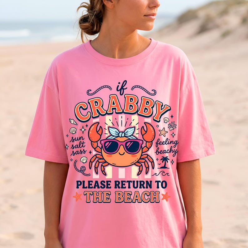 May include: A pink t-shirt featuring a cartoon crab wearing sunglasses and a bow. The text on the shirt says "if crabby, please return to the beach." The design includes stars, shells, and a palm tree.