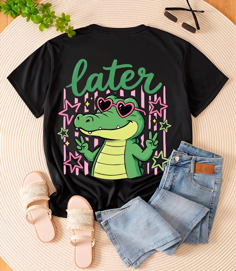 May include: Black t-shirt with a cartoon alligator wearing heart-shaped sunglasses and the word "later". The alligator is green and the sunglasses are pink. The shirt is paired with light wash denim jeans and pink sandals.