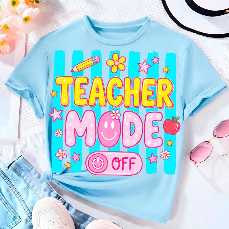 May include: Light blue t-shirt with the words "TEACHER MODE OFF" in a colorful design. The shirt features a pencil, flowers, stars, and an apple graphic. The shirt is made of a soft material and is suitable for casual wear.