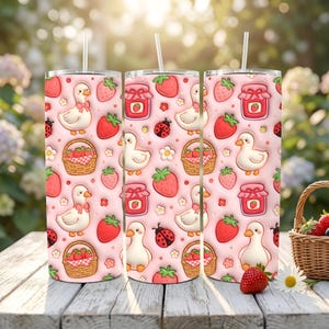 Op de afbeelding: Drie roestvrijstalen bekers met een roze achtergrond met een herhalend patroon van witte eenden, aardbeien, aardbeienjam potten, lieveheersbeestjes en manden met aardbeien. Elke beker heeft een wit rietje.