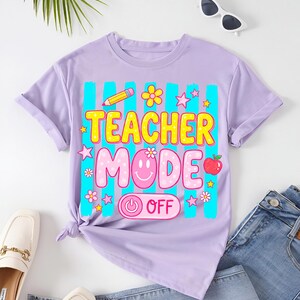 May include: A lilac-colored t-shirt with the words "TEACHER MODE OFF" in a colorful, playful font. The design includes a pencil, flowers, stars, a smiling face, and an apple. The shirt is styled with jeans and loafers.