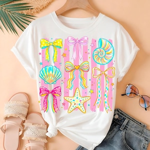 May include: White t-shirt featuring a colorful design of bows, seashells, and a starfish. The design includes pink and white striped vertical lines. The shirt is paired with sandals and blue jeans.