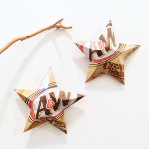 May include: Two brown and white paper stars with the A&W Root Beer logo and the text "Cream Soda" hanging from a branch.