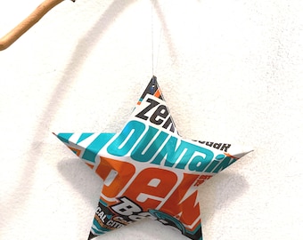May include: A five-pointed star ornament crafted from recycled soda can aluminum. The surface features vibrant orange, bright teal, white, and black graphics with visible text including Mountain Dew branding, suspended by a thin silver string.
