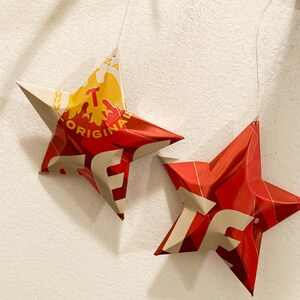 May include: Two red and white star-shaped ornaments made from recycled aluminum cans. The larger star has the text "ORIGINAL" and "TEQUILA" on it.