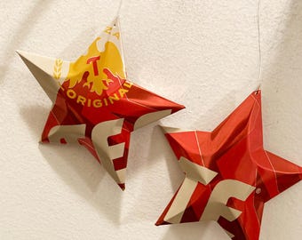 May include: Two red and white star-shaped ornaments made from recycled aluminum cans. The larger star has the text "ORIGINAL" and "TEQUILA" on it.