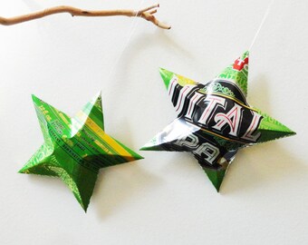 May include: Two green and yellow star-shaped ornaments made from recycled aluminum cans. The larger star has the words "Vital Pale" printed on it. The smaller star has text that is too small to read.