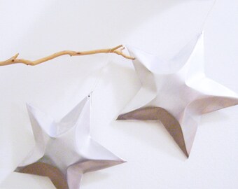 May include: Two silver origami stars hanging from a branch against a white background.