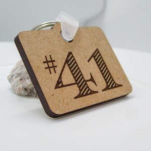 May include: A wooden keychain with the number 41 engraved on it. The number is in a black font with a striped pattern. The keychain is brown and has a metal ring.