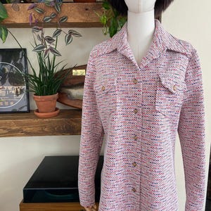 May include: A long-sleeved button-down shirt featuring a textured weave in a multi-coloured pattern of white, red, and blue threads. The shirt includes a pointed collar, two chest pockets with buttoned flaps, and a front placket with round buttons.