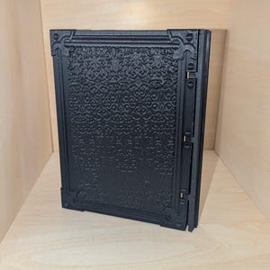 May include: A black, decorative, hinged box with a detailed, embossed pattern on the front.