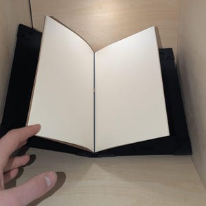 May include: A black book stand with a white book resting on top. The book is open and the pages are blank.