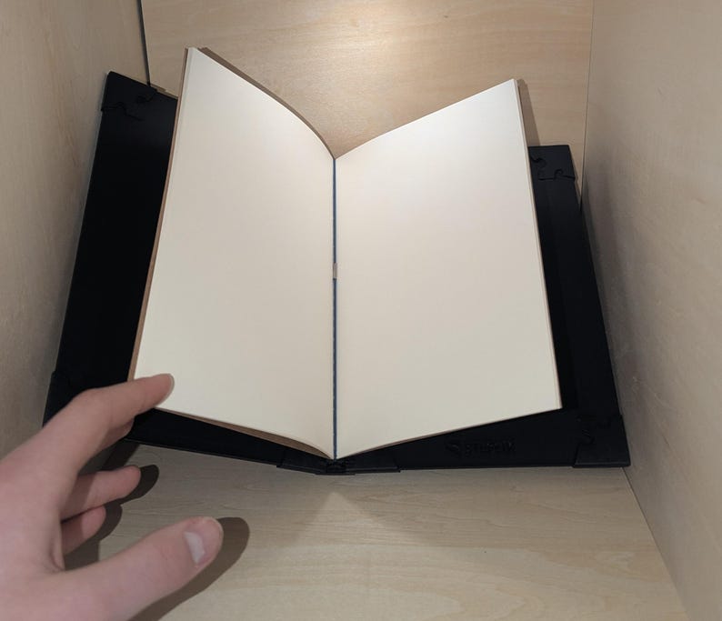 May include: A black book stand with a white book resting on top. The book is open and the pages are blank.