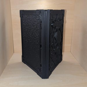 May include: A black, intricately designed, 3D printed book with a skull embossed on the front cover.