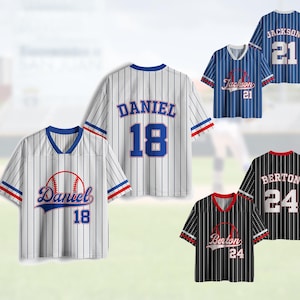 May include: Baseball jerseys in white, blue, and black with vertical stripes. Each jersey features a player's name and number, with details like a baseball graphic and contrasting sleeve trim. The jerseys have a V-neck design.