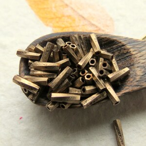 Puede incluir: Una cuchara de madera llena de cuentas de metal doradas. Las cuentas son hexagonales y tienen un acabado ligeramente texturizado.