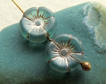 Puede incluir: Dos cuentas de vidrio de color azul turquesa con un diseño de estrella plateada. Las cuentas están enhebradas en un alambre dorado.
