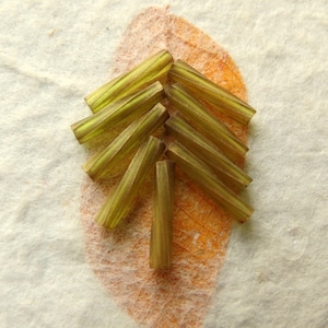 May include: A group of 10 green glass beads with a striated texture. The beads are arranged in a triangular shape on a white surface.