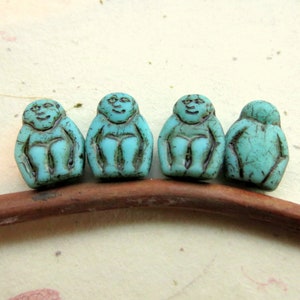 May include: Four turquoise blue glass beads shaped like sitting figures with distressed detailing.