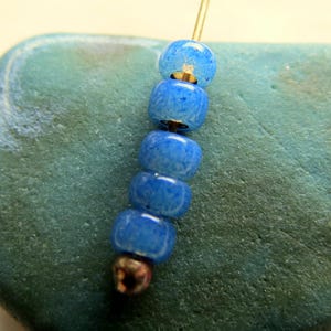 May include: A close-up of a strand of blue beads with a gold-colored wire. The beads are a vibrant blue color and have a textured appearance. The beads are strung together, creating a decorative element.