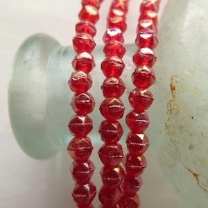May include: A strand of red iridescent glass beads. The beads are faceted and have a shiny finish.