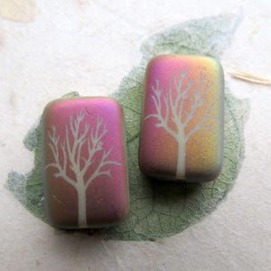 Puede incluir: Dos azulejos de vidrio rectangulares con un diseño de árbol blanco. Los azulejos tienen un acabado iridiscente rosa y naranja.