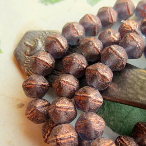 May include: A strand of copper-toned glass beads with a faceted, geometric shape. The beads have a textured, metallic finish and are strung on a silver-colored wire.