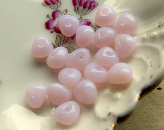 May include: A collection of pale pink glass beads in a heart shape. The beads are arranged on a white plate with a floral design.