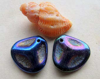 May include: Two iridescent blue glass triangle shaped beads with a hole at the top. The beads have a metallic sheen and are next to a small seashell.