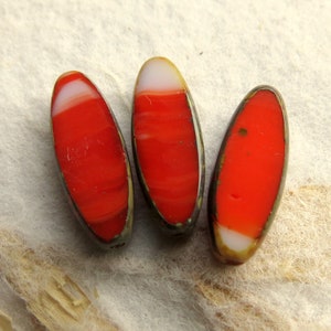May include: Three oval-shaped glass beads with red and white stripes. The beads have a metallic sheen and are arranged in a row.