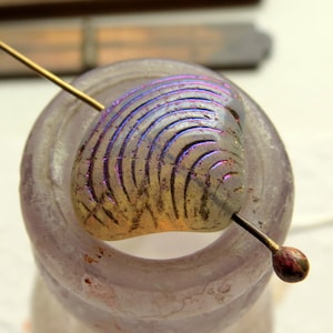 May include: A iridescent glass bead with a textured, circular pattern. The bead is threaded on a gold wire.