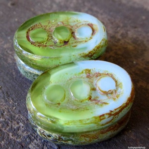 May include: Two green and white glass buttons with three holes each. The buttons have a mottled, aged appearance.