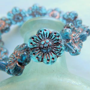 May include: A turquoise blue flower-shaped glass bead bracelet with copper accents. The bracelet is made of multiple beads that are strung together.