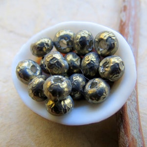 Puede incluir: Primer plano de un montón de pequeñas cuentas redondas y metálicas en una concha blanca. Las cuentas son de color gris oscuro con un brillo metálico.