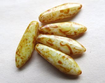 May include: Six white glass beads with brown marbling. The beads are long and narrow, resembling rice grains.