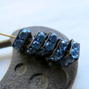 Op de afbeelding: Een close-up van een blauw strass sieraad met een zilveren metalen basis. De strass steentjes zijn in een spiraalvorm gerangschikt.