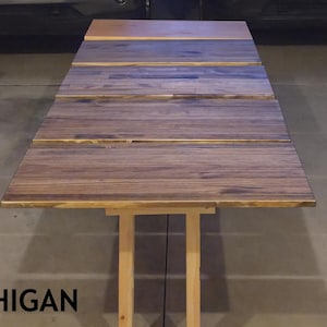 May include: Three wooden tables with different finishes are displayed. The tables are rectangular and have a rustic appearance. The text "HANDMADE IN MICHIGAN" is at the bottom of the image.
