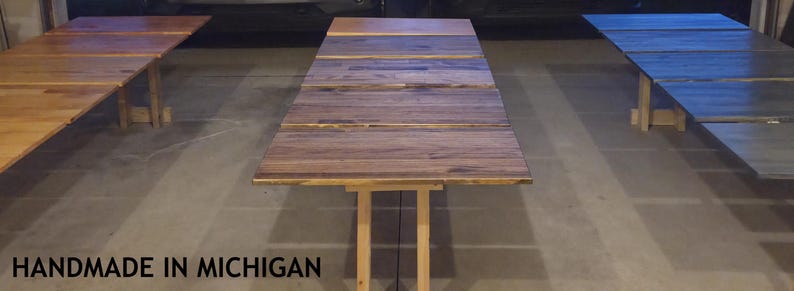 May include: Three wooden tables with different finishes are displayed. The tables are rectangular and have a rustic appearance. The text "HANDMADE IN MICHIGAN" is at the bottom of the image.
