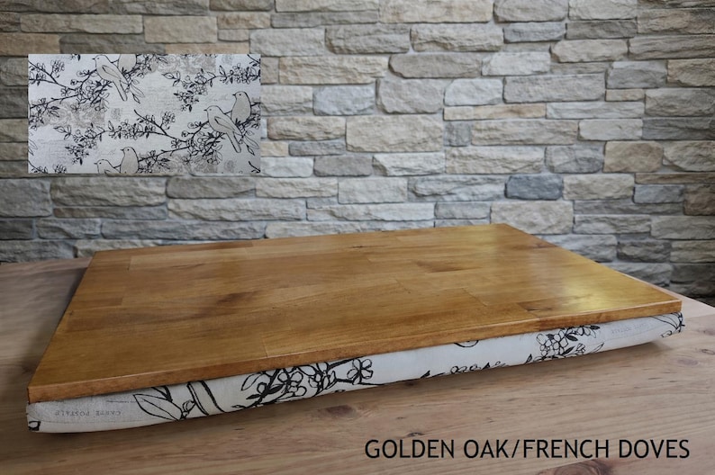 May include: A rectangular wooden lap desk with a golden oak finish. The base is covered in fabric with a black and white bird and floral pattern. The text "GOLDEN OAK/FRENCH DOVES" is at the bottom.