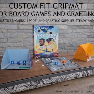 May include: A wooden board game surface with the text "CUSTOM FIT GRIPMAT FOR BOARD GAMES AND CRAFTING". The image shows a board game box, dice, and game pieces. The surface is designed to keep game tiles, cards, and crafting supplies steady.