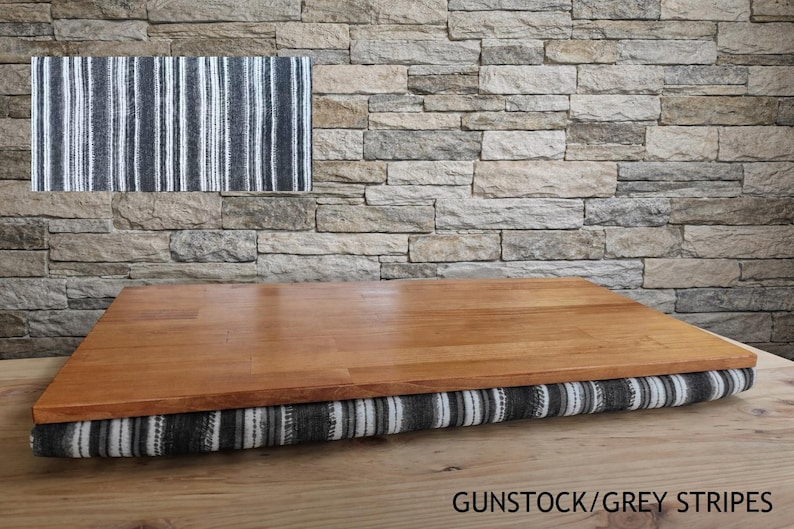 May include: A wooden laptop desk with a striped cushion base. The desk has a light brown wooden surface and a cushion with vertical stripes in shades of gray and white. The text "GUNSTOCK/GREY STRIPES" is visible at the bottom.