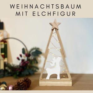 Könnte beinhalten: Weihnachtsbaum aus Holz mit Sternaufsatz und weißer Rentiersilhouette im Inneren. Der Baum ist mit kleinen, warmweißen Lichtern beleuchtet. Der Text oben lautet "WEIHNACHTSBAUM MIT ELCHFIGUR".