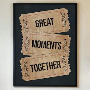 Puede incluir: Impresión enmarcada con tres boletos de estilo vintage. Los boletos, en tonos beige, están dispuestos verticalmente y dicen "GREAT", "MOMENTS" y "TOGETHER" en texto negro en negrita. La impresión está sobre un fondo azul oscuro.