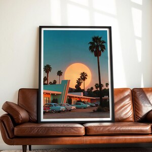 May include: A framed print depicting a retro motel scene at sunset. The image features palm trees, vintage cars, and a large sun. The motel has a teal and white color scheme, and the sky is a gradient of blue and orange.