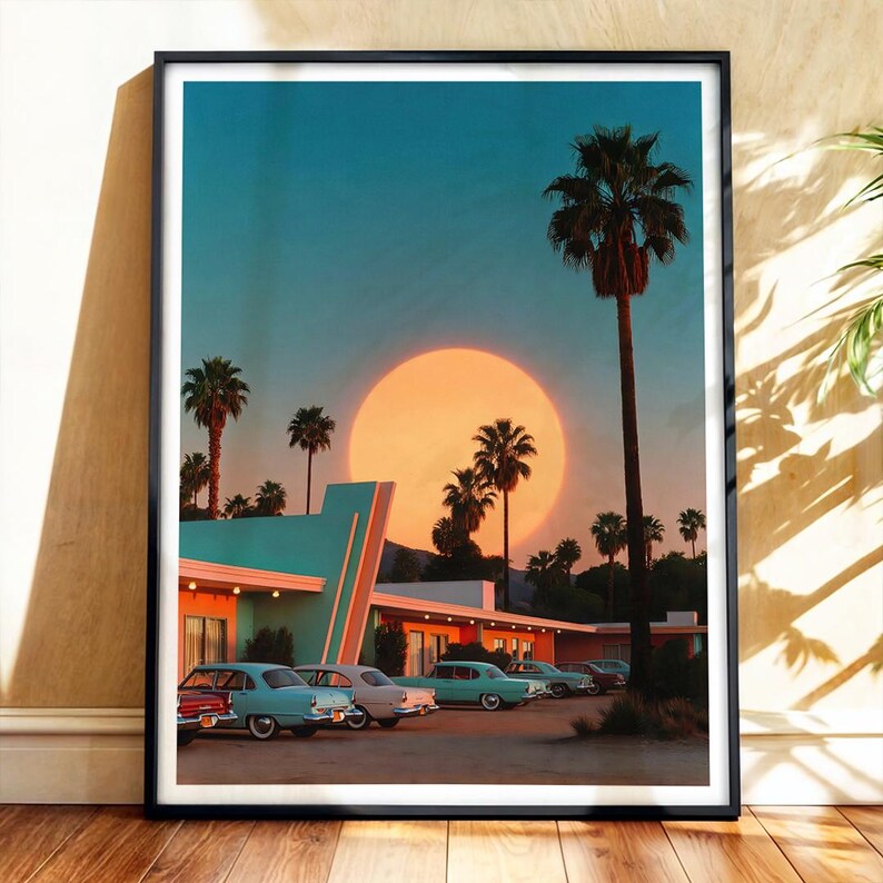 May include: Framed art print featuring a retro motel scene at sunset. The image showcases a teal and coral building with vintage cars parked in front. Palm trees and a large orange sun dominate the background, creating a nostalgic, vintage aesthetic.